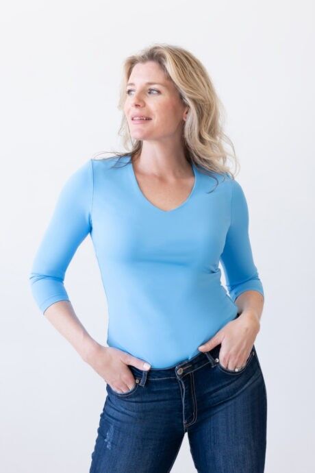 A woman wearing jeans and a blue V-Neck ¾ Sleeve Top, standing confidently.